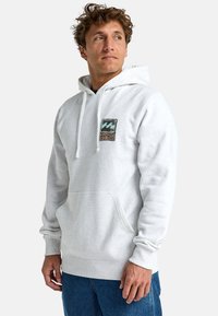 Light gray hooded sweatshirt with a kangaroo pocket. Features a colorful graphic patch on the chest and ribbed cuffs and hem.