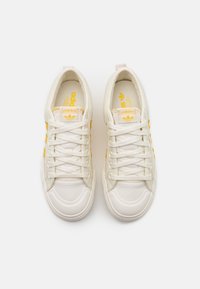 Vita canvas sneakers med gula accenter, med runda gummitå, platta snören och en logotyp på plösen och innersulan.