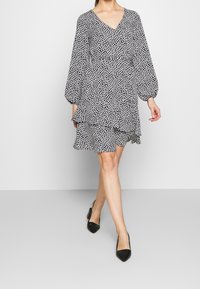 Black and white patterned dress with a V-neck, long puff sleeves, and a ruffled hem, paired with black pointed-toe heels.