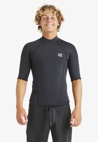 Czarna krótka koszulka rash guard z elastycznego materiału, z wysokim kołnierzem, z białym logo na klatce piersiowej i płaskimi szwami.