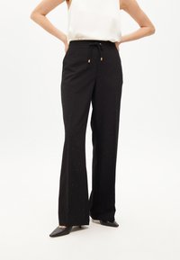 Čierne rozšírené nohavice s pásom na šnurovanie, s jemnými kovovými klincami roztrúsenými po látke. Hladká textúra, doplnené čiernymi podpätkami.