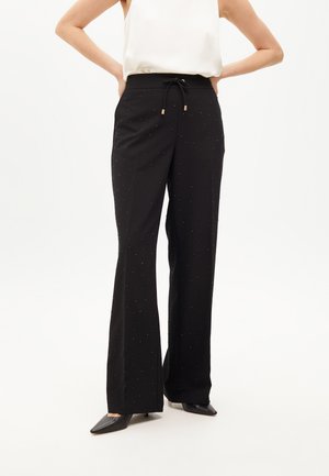 Black flared trousers with a drawstring waistband, featuring subtle metallic studs scattered throughout the fabric. Smooth texture, paired with black heels.