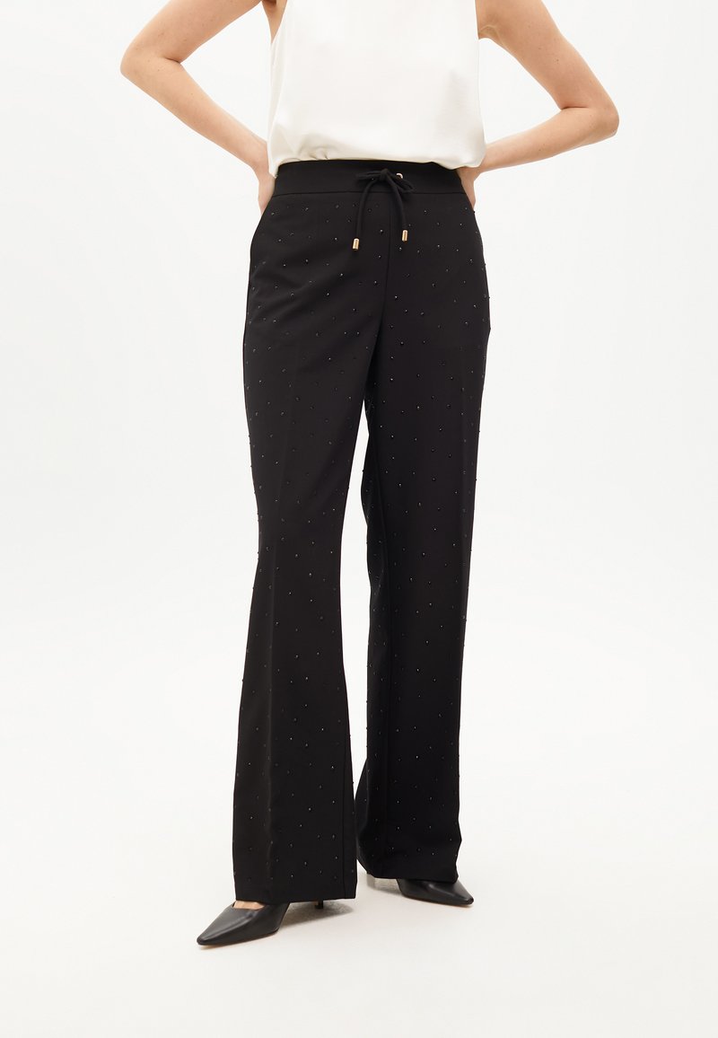 Čierne rozšírené nohavice s pásom na šnurovanie, s jemnými kovovými klincami roztrúsenými po látke. Hladká textúra, doplnené čiernymi podpätkami.