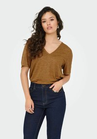 Bruine V-hals T-shirt met korte mouwen, gecombineerd met high-waisted donkerblauwe jeans. Het T-shirt heeft een zachte textuur en een ontspannen pasvorm.