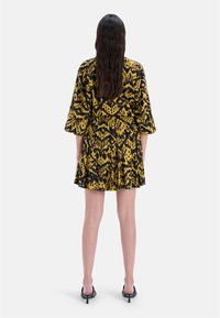 Żółto-czarna sukienka w wzór, z rozkloszowanym dołem, rękawami do trzech czwartej długości i elastycznym pasem, wykonana z lekkiego materiału.