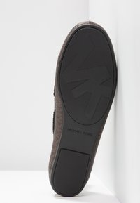 Semelle d'une chaussure Michael Kors marron avec grip texturé en caoutchouc noir et grand logo "MK" sur la zone avant du pied.