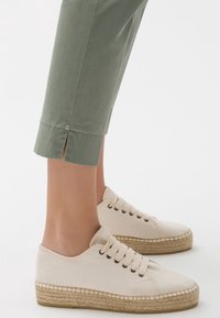 Vita canvas sneakers med espadrillastil jutesulor och förstärkta öglor för snörning; bärs med ljusgröna avkapade byxor med sidofickor.
