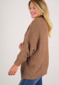 Chunky gebreide trui in lichtbruin met een losse pasvorm, geribde manchetten en zoom. Beschikt over een gestructureerd patroon en verlaagde schouders.