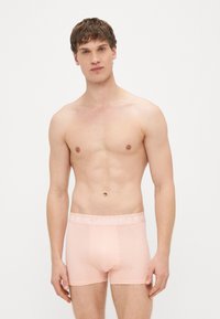 Boxer en coton pêche avec une texture lisse, doté d'une ceinture blanche de marque et d'une coupe ajustée.