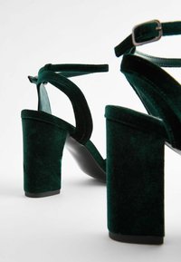 Gröna sammetshögklackade sandaler med breda blockklackar, justerbara ankelremmar och släta svarta sulor. Det texturerade materialet har ett rikt utseende.