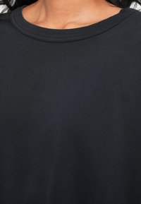 Μαύρη βαμβακερή μπλούζα με στρογγυλή λαιμόκοψη, λεία υφή και κοντά μανίκια, με διακριτές ραφές γύρω από την κολλέτα.