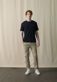 Melna crew-neck t-krekla, beigu chinos un baltas sporta apavus. Audums ir gluds; fit ir ikdienešs un taisns. Vienkāršs dizains bez rakstiem.
