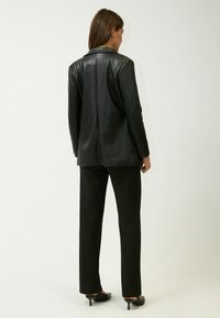 Blazer in pelle nera con un design strutturato, colletto a revers e spacco posteriore. Abbinato a pantaloni neri e tacchi, creando un look monocolore.