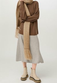 Pull marron côtelé, écharpe beige en tricot avec franges, jupe grise longueur genou, et bottines beiges avec semelles noires. Look décontracté superposé.