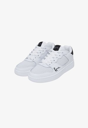 Baskets blanches en matière synthétique perforée, avec des lacets plats et un accent noir au talon, ornées d'une signature noire sur le côté.