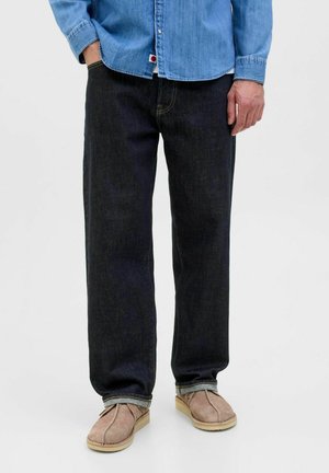 Dunkelblaue gerade Jeans mit glatter Textur, kombiniert mit beigefarbenen Wildlederschuhen. Das Outfit beinhaltet ein hellblaues Jeanshemd.