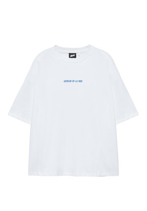 Hvid oversize t-shirt med korte ærmer og blå tekst "L'AMOUR DE LA MER" trykt midt foran.