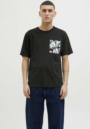 Sorte bomulds T-shirt med rund hals, som har en mønstret lomme i hvid og grå nuancer. Kombineret med mørkeblå denim jeans.