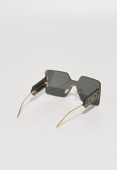 Lunettes de soleil noires carrées, accents en métal doré et design de cadre géométrique unique. Les verres sont teintés en gris foncé avec un détail de logo sur les branches.