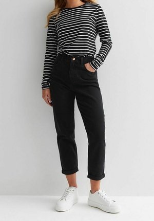 Femme portant une chemise à manches longues rayée noir et blanc, un pantalon noir taille haute roulé et des baskets blanches à plateforme.