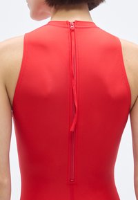 Κόκκινο ολόσωμο μαγιό χωρίς μανίκια με ψηλό λαιμό και φερμουάρ στην πλάτη. Ομαλό, ελαστικό υλικό με εφαρμοστή σιλουέτα.