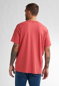 Korte mouwen, ronde hals t-shirt van zacht koraalstof. Kenmerkt zich door een comfortabele pasvorm en subtiele stikseldetails. Gepaard met blauwe jeans.