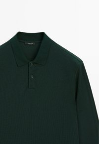 Donkergroene polo met lange mouwen gemaakt van een gestructureerde stof, drie knoopsluiting en een klassieke platte kraag. Minimale branding aan de binnenkant van de kraag.