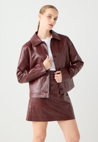 Bordeaux neplederen jack met een kraag, knoopsluiting en lange mouwen, gecombineerd met een bijpassende minirok. Gladde textuur.