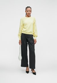 Lys gul genser med øyesøm på puffermene, parret med grå høyt midje bukser og svarte spisse sko. Hvit veske.