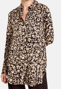 Blusa nera con motivo floreale in crema e beige. Presenta una chiusura frontale con bottoni, maniche lunghe e una vestibilità morbida per il massimo comfort.