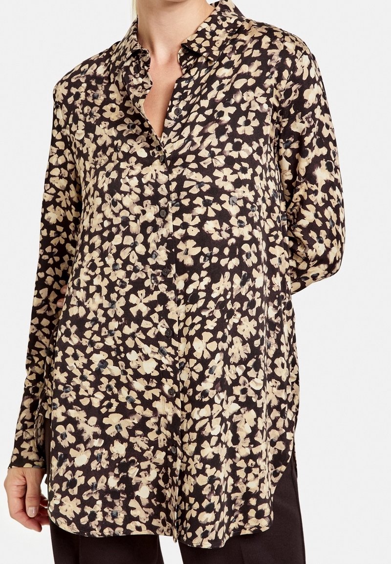 Blusa nera con motivo floreale in crema e beige. Presenta una chiusura frontale con bottoni, maniche lunghe e una vestibilità morbida per il massimo comfort.
