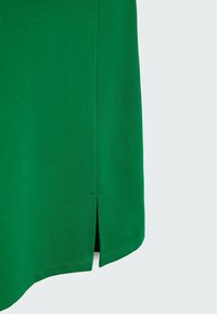Grøn bomulds t-shirt med afrundet kant og sideslids. Har en glat tekstur og pæne syninger langs kanterne.
