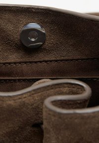 Interior de una bolsa de ante marrón con un cierre a presión de botón oscuro y suave, mostrando una tela texturizada y una costura a lo largo del borde.