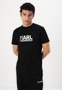 Μαύρη βαμβακερή μπλούζα με κοντό μανίκι και κανονική λαιμόκοψη. Διαθέτει μεγάλο λευκό λογότυπο "KARL LAGERFELD" μπροστά. Λείος υφασμάτινος τύπος.