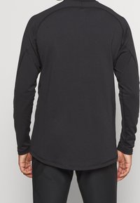 Svart långärmad träningsskjorta med rundad nederkant, platta sömmar och en figurnära design. Tillverkad av fukttransporterande material för aktiv användning.