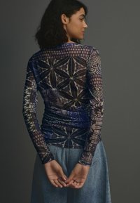 T-shirt en mesh à manches longues présentant une variété de motifs complexes dans des tons de bleu et de violet, avec des détails froncés à la taille.