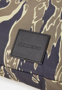 Tessuto a motivo camouflage con una miscela di beige, verde scuro e blu navy. Presenta un'etichetta in pelle nera impresso con "ALLSAINTS".