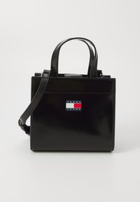 Sac à main en cuir verni noir avec deux poignées sup�érieures, une bandoulière réglable et un patch logo à l'avant aux couleurs bleu, rouge et blanc.