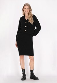 Schwarzes Strick-Set mit einem V-Ausschnitt, kurz geschnittenem Cardigan mit Knopfleiste und einem knielangen Rock, beide mit einem strukturierten Rippmuster.