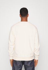 Helles Creme Sweatshirt mit Rundhalsausschnitt, gerippten Bündchen und Saum sowie einer weichen Textur, kombiniert mit dunklen Jeans.