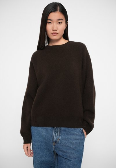 Brun løstsiddende sweater med rund hals, ribbede manchetter og kant. Sammen med blå jeans. Blød tekstur, minimalistisk design.