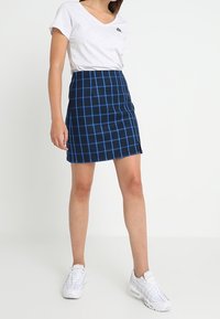 Mini falda a cuadros azul y negra hecha de un tejido suave, con una abertura lateral y un diseño ajustado, combinada con una camiseta de cuello en V de color gris claro.