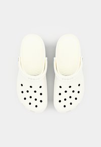 Vita Crocs-tofflor med en strukturerad design, 13 runda svarta ventilationshål och justerbar hälrem för en säker passform.