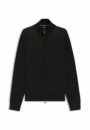 Svart cardigan med dragkedja framtill, stickad struktur och ribbade ärmslut. Enfärgad med ett subtilt mönster på den övre frampanelen.