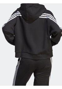 Svart croppad hoodie i mjukt material, utrustad med huva och tre vita ränder längs axlarna, tillsammans med matchande svarta byxor.