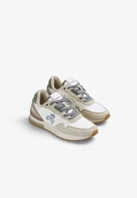 Zapatillas deportivas de ante blancas y beige con cordones grises, que presentan un logo de calavera en el lateral y suelas de goma con un acabado texturizado.