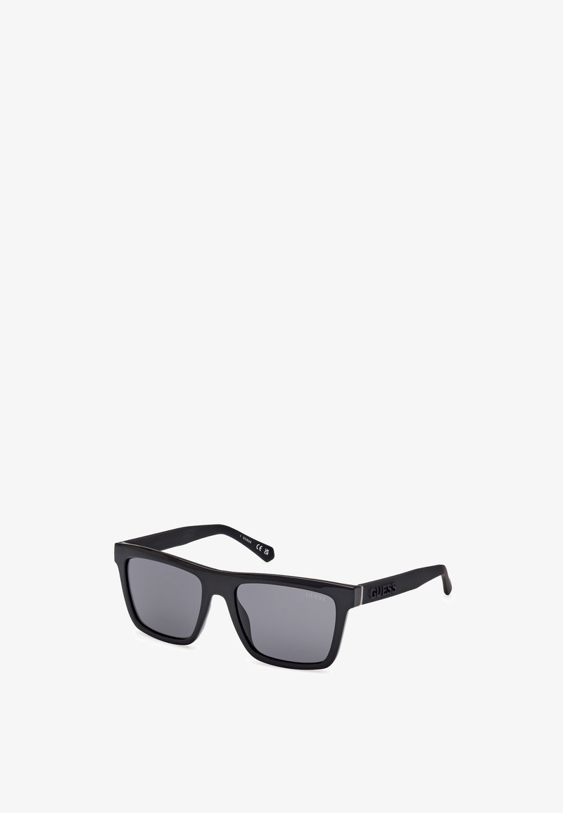 Óculos de sol retangulares pretos com lentes escuras, acabamento mate e detalhe do logótipo na haste. O design apresenta arestas retas e aros grossos.