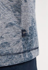 Texturovaná tkanina v námořnické a světle modré barvě se vzorem a olemovaným okrajem; obsahuje malou černou štítku s logem.