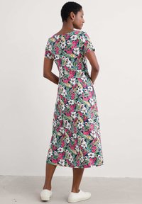 Cvečni midi plašč s kratkimi rokavi, z mornarsko modro podlago, živahnimi rožnatimi in belimi cvetovi ter sproščenim krojem. Gladka tkanina in dolžina do kolen.