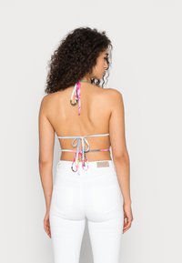 Top halter multicolor com tiras finas em rosa, azul e prata; amarrado no pescoço e nas costas, combinado com calças brancas de cintura alta.